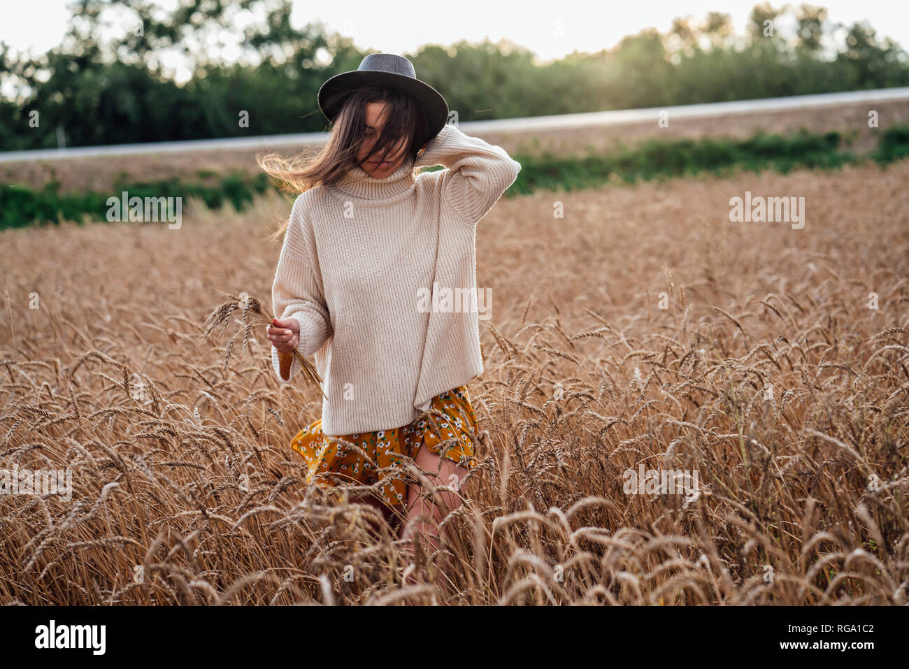 Young woman wearing hat and oversized turtleneck pullover walking in corn field Stock Photo