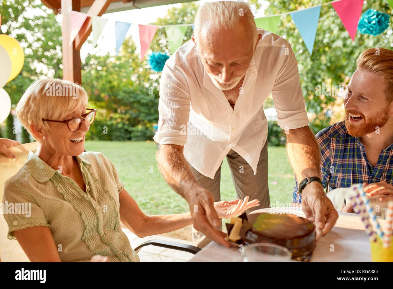 Senior man serving cake on a garden party Stock Photo