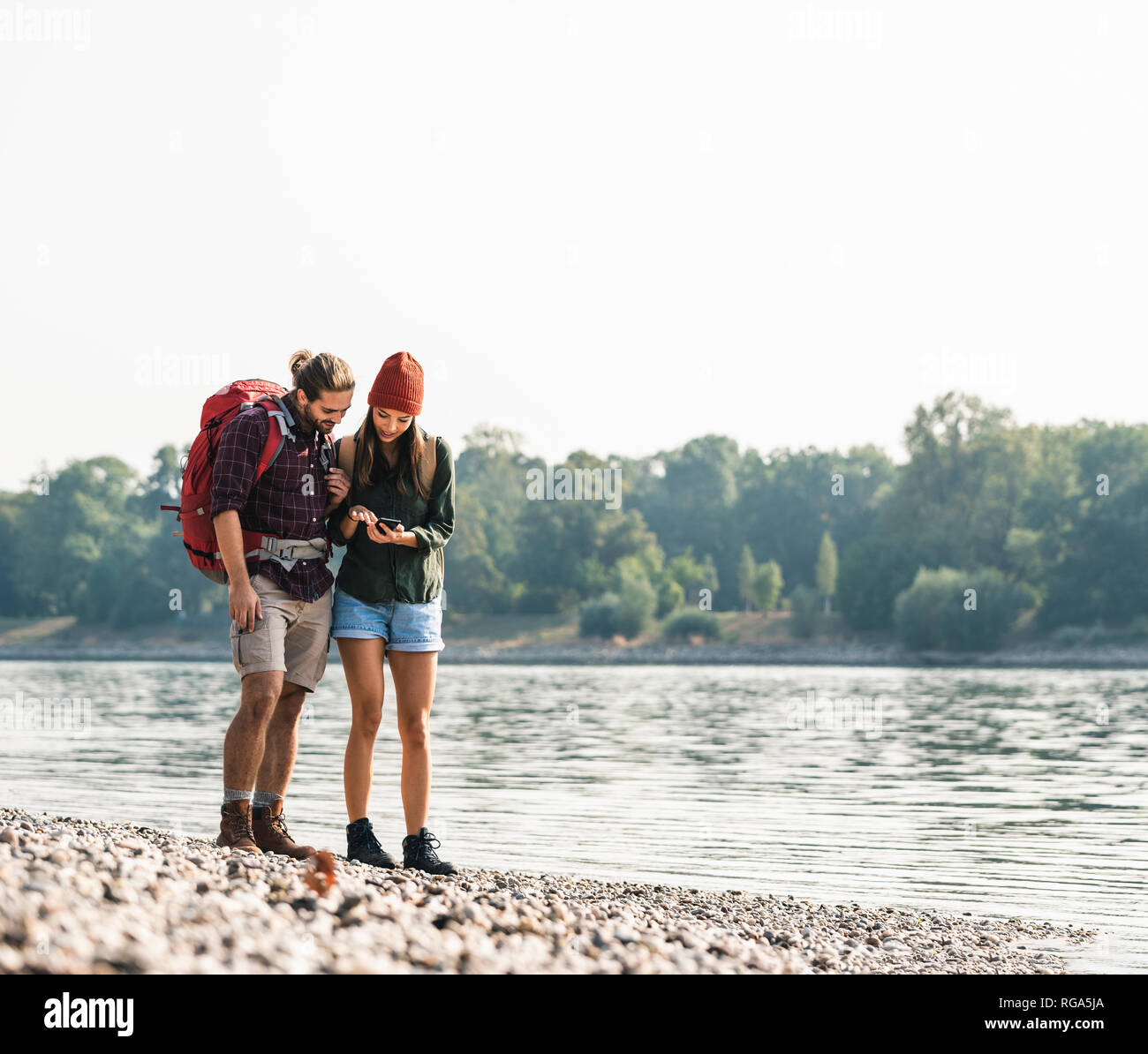Young couple with backpacks at the riverside checking cell phone Stock Photo