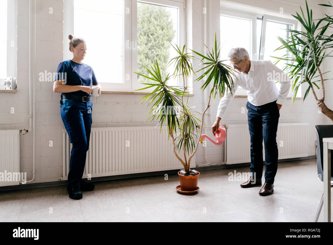 Manager watering plants in recreation room, while worker is drinking coffee Stock Photo