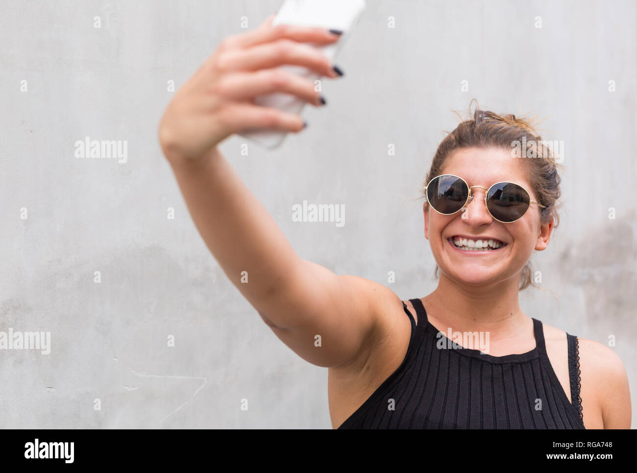 Portrait of laughing young woman wearing sunglasses taking selfie with smartphone Stock Photo
