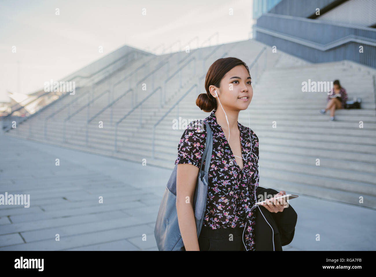 Smiling Asian student listening to music while walking on campus Stock Photo