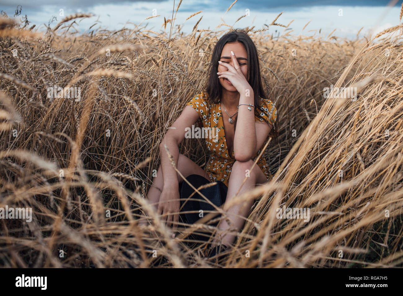 Laughing young woman with hand on face sitting in corn field Stock Photo