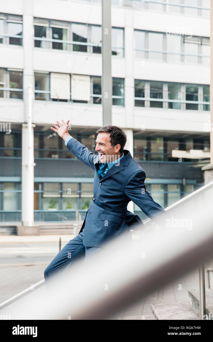 Carefree businessman sliding down railing in the city Stock Photo