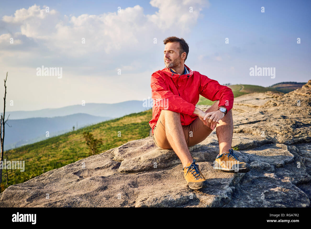 Man sitting on rock enjoying serene moments during hiking trip Stock Photo