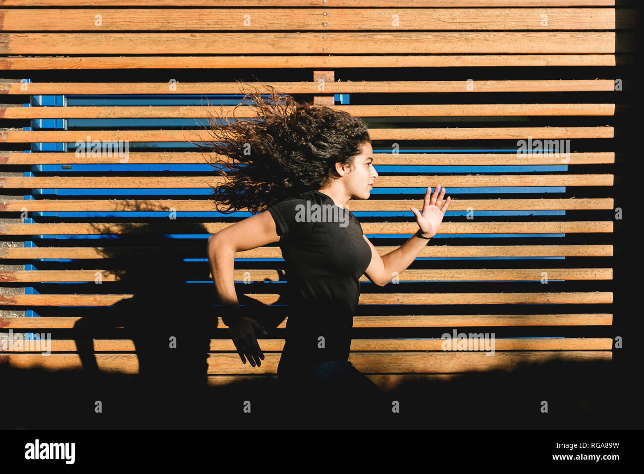 Sportive young woman running along wood paneling Stock Photo