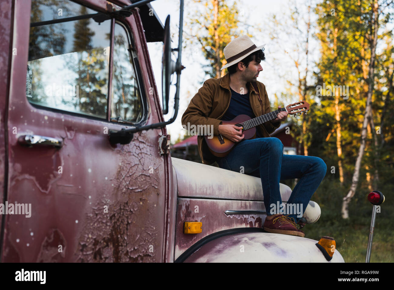 Young amn sitting on a broken truck, playing the ukulele Stock Photo