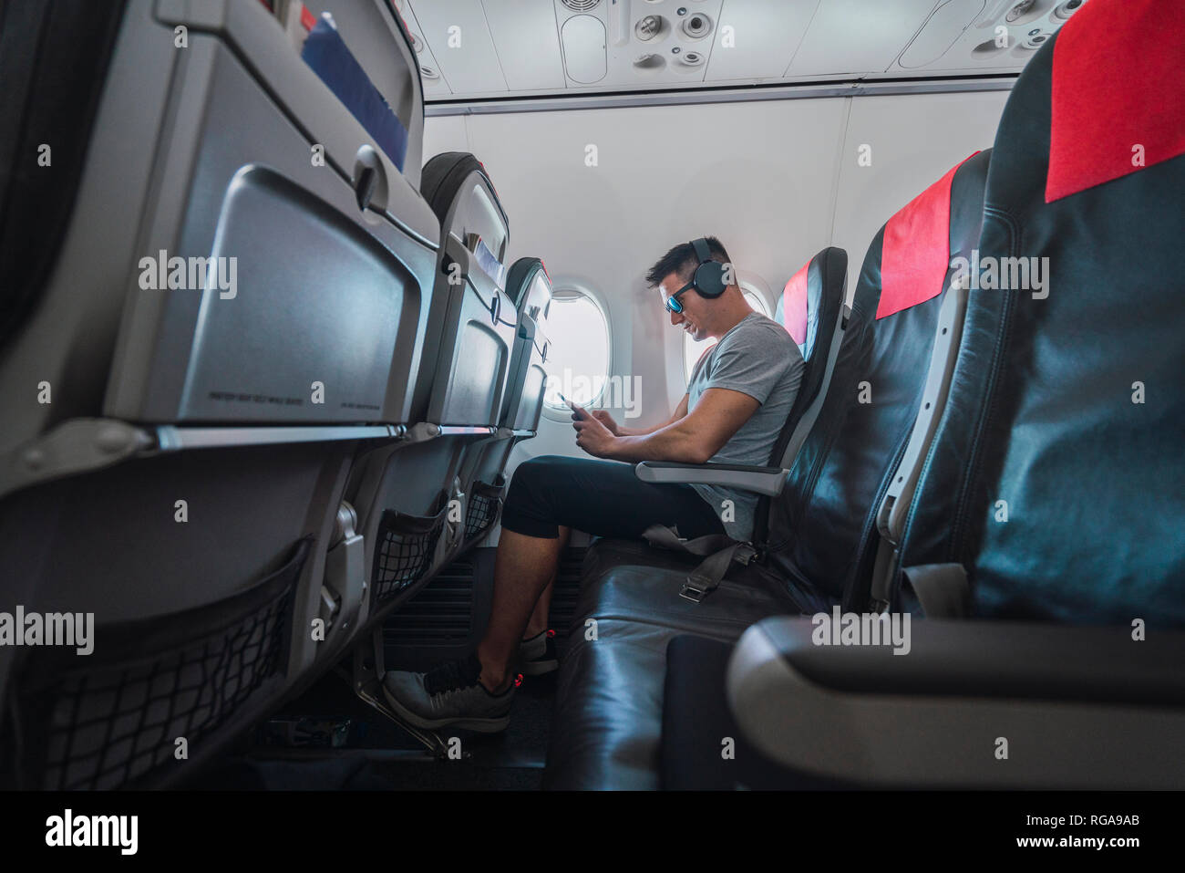 Man in airplane, using smartphone, headphones Stock Photo