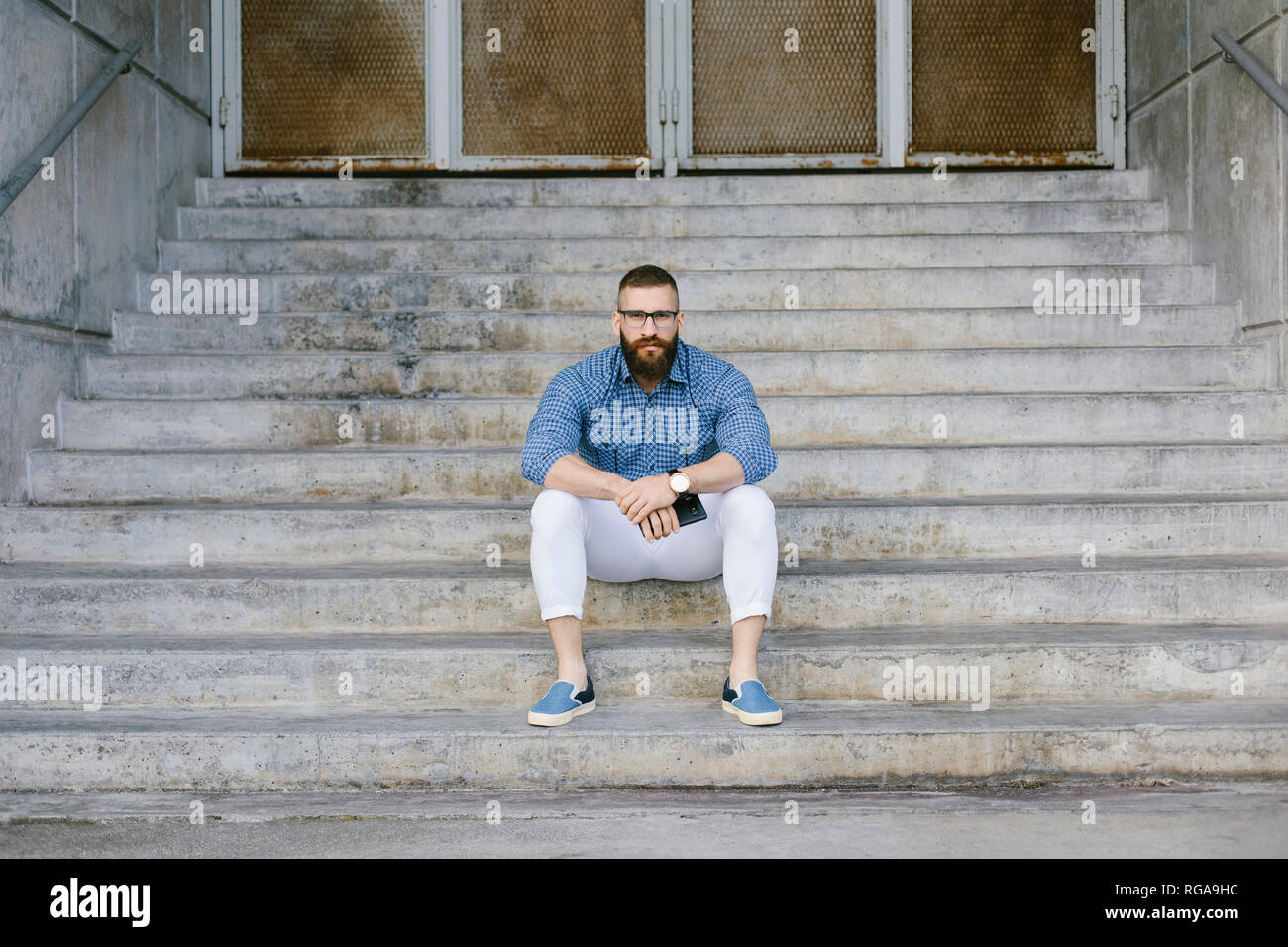 Portrait of bearded hipster businessman with smartphone sitting on stairs Stock Photo