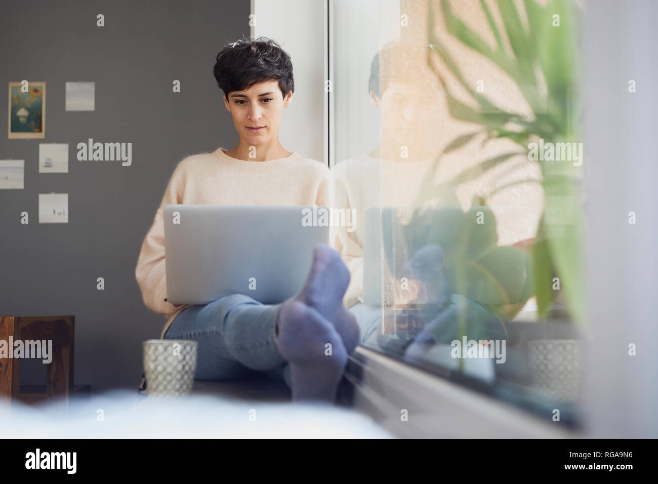Woman at home sitting at the window using laptop Stock Photo
