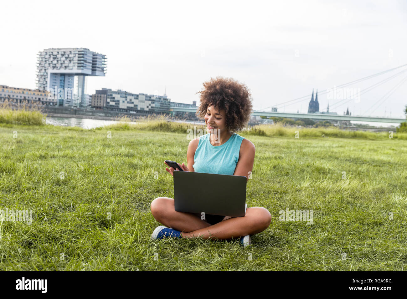 Germany, Cologne, woman sitting on meadow using laptop and cell phone Stock Photo