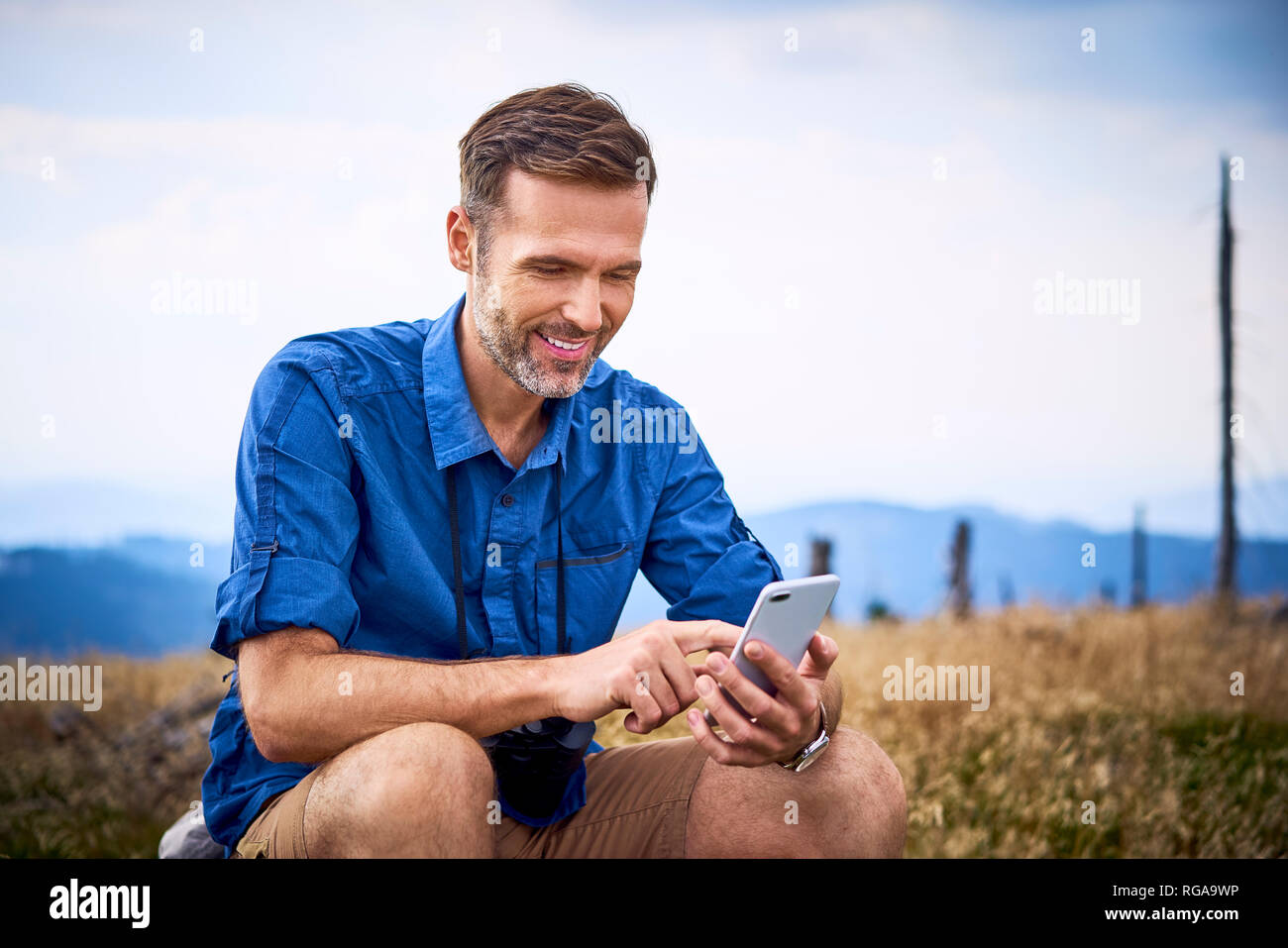 Smiling man resting and checking his cell phone during hiking trip Stock Photo
