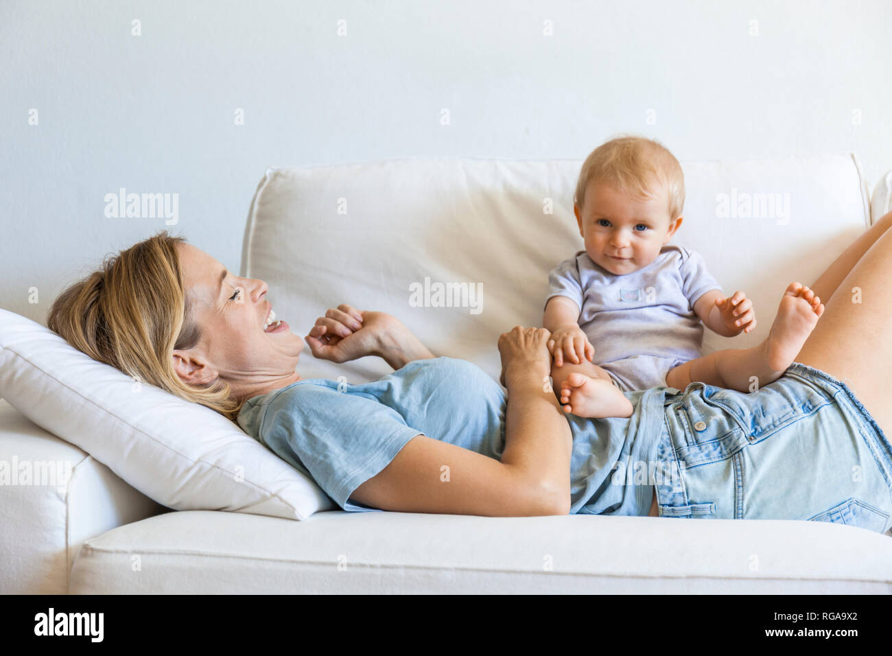 Happy mother lying on couch with her baby girl Stock Photo