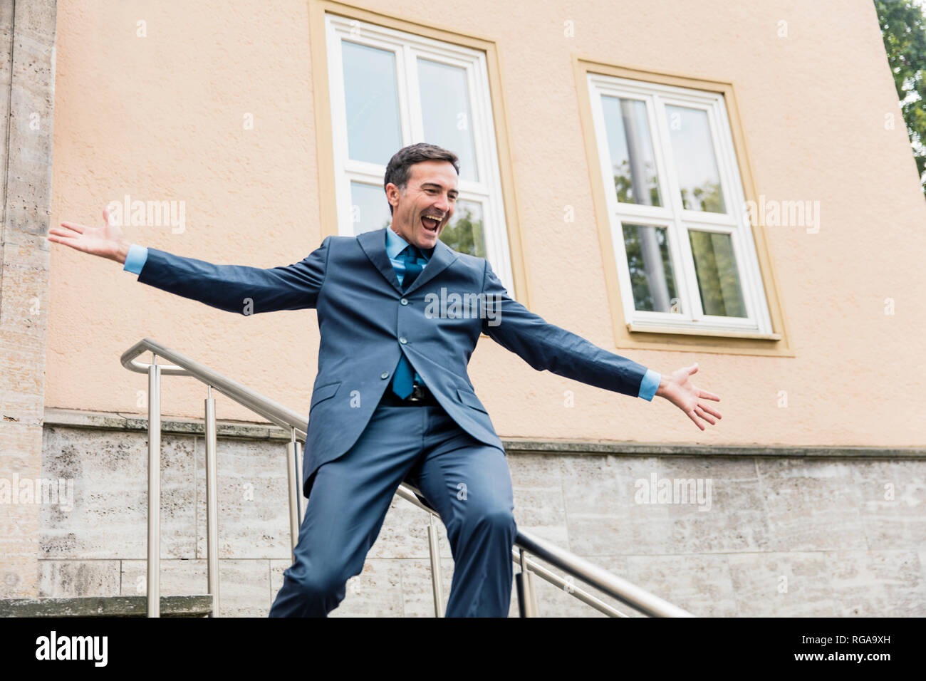 Carefree businessman sliding down railing in the city Stock Photo