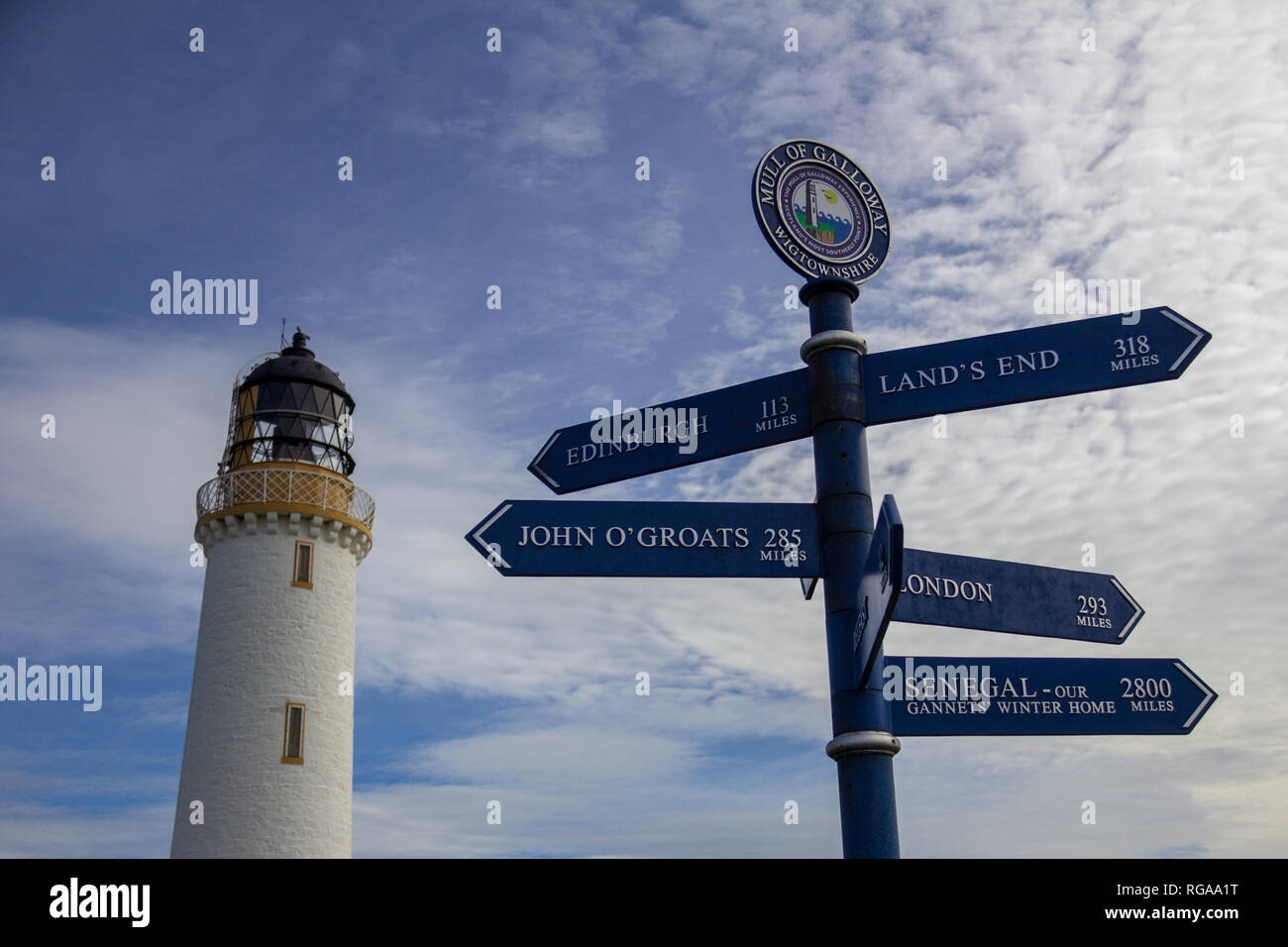 Sign post in front of the Mull of Galloway lighthouse in Dumfries and Galloway, Scotland, United Kingdom under a blue sky with white clouds Stock Photo