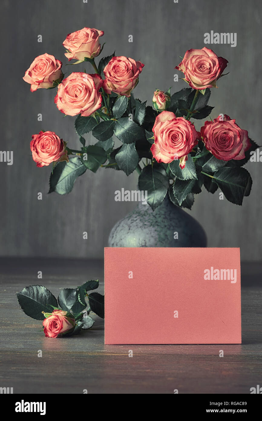 Bouquet of pink roses and a blank pink paper card on dark rustic ...