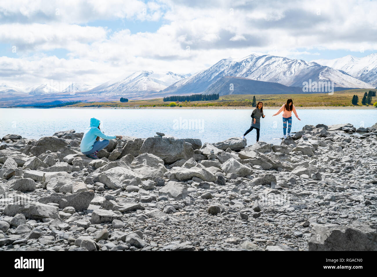 LAKE TEKAPO NEW ZEALAND - OCTOBER 14 2018; three young tourists  enjoy experience of rocky foreshore of low water level at lake edge Stock Photo