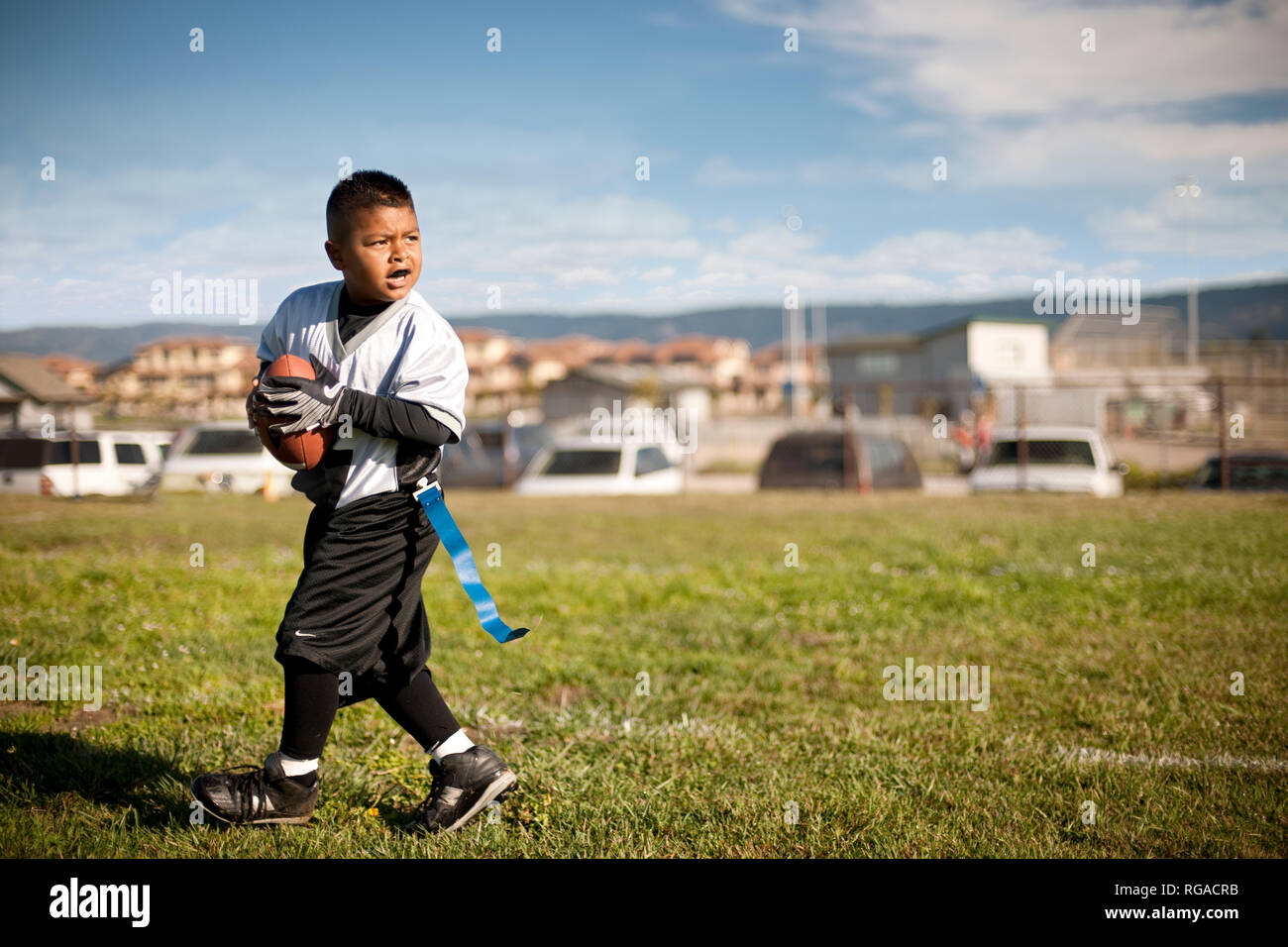 Boy carrying a football while wearing an over sized sports uniform on a sports field. Stock Photo