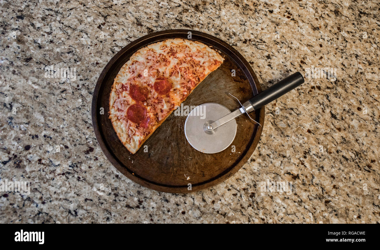 Half of a leftover frozen pizza discarded on the counter top. Stock Photo