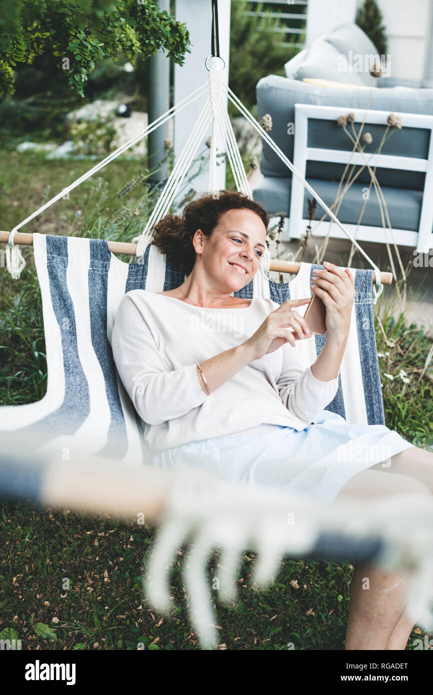 Smiling woman lying in a hammock using cell phone Stock Photo - Alamy