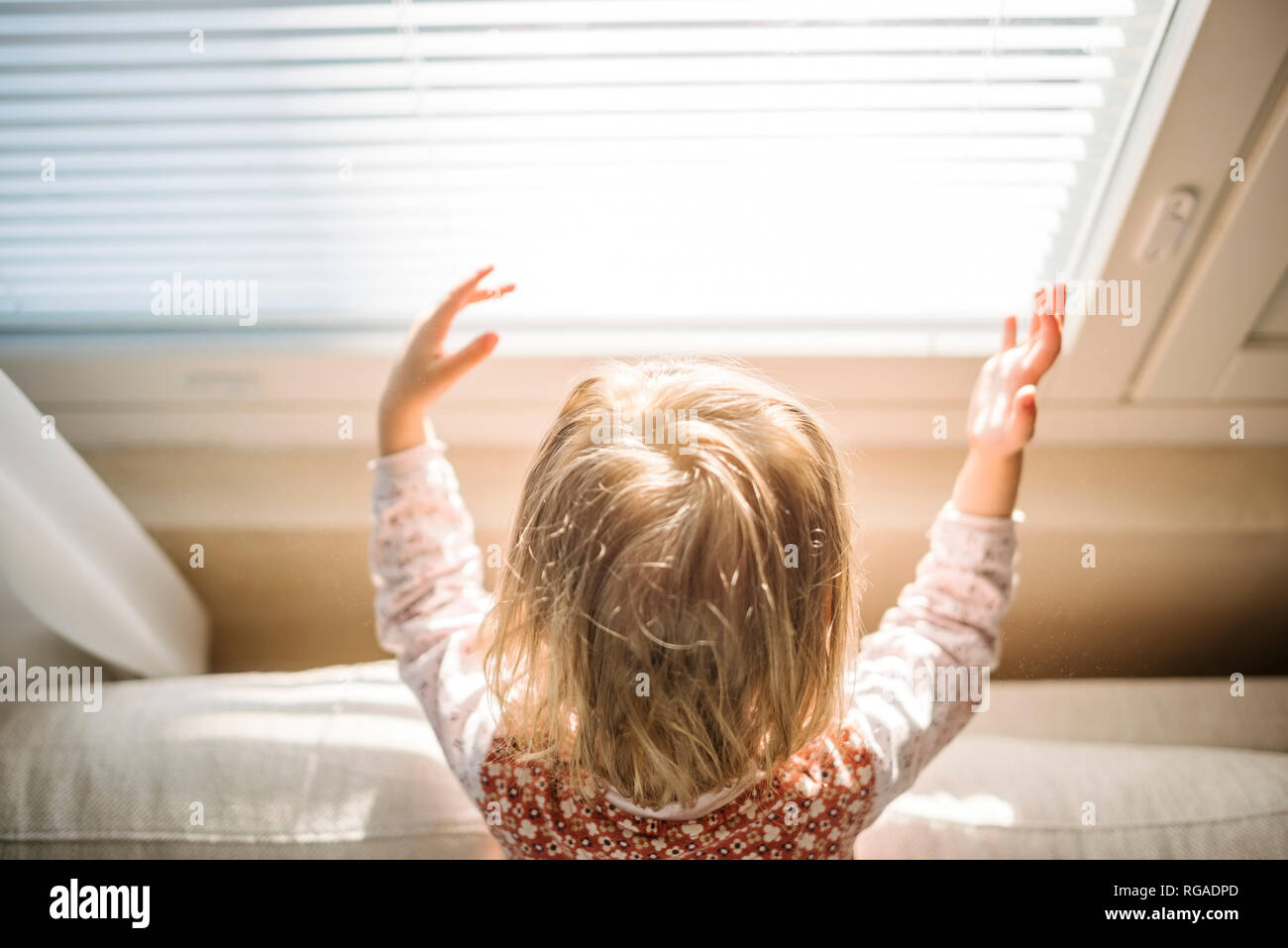 Back view of blond little girl at window playing with sunlight Stock Photo