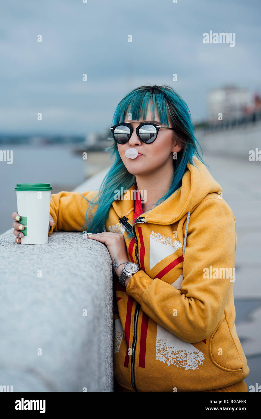 Portrait of young woman with dyed blue hair wearing mirrored sunglasses and fashionable hooded jacket Stock Photo