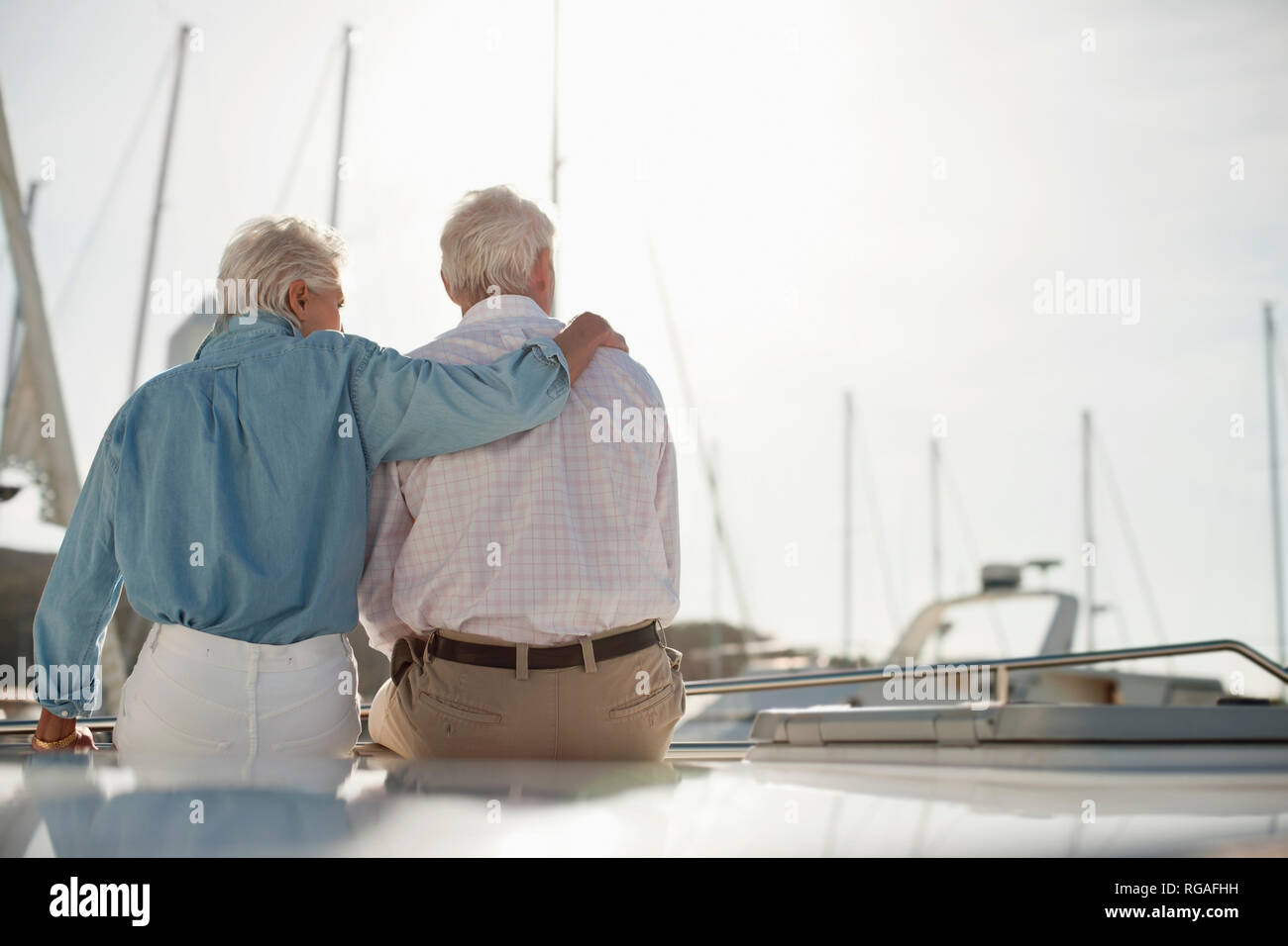 Senior woman puts her hand around her husband's shoulders as they sit on a boat looking out over the marina. Stock Photo