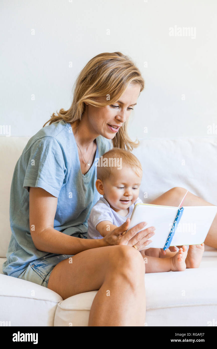 Mother and baby girl sitting on couch looking at picture book Stock Photo