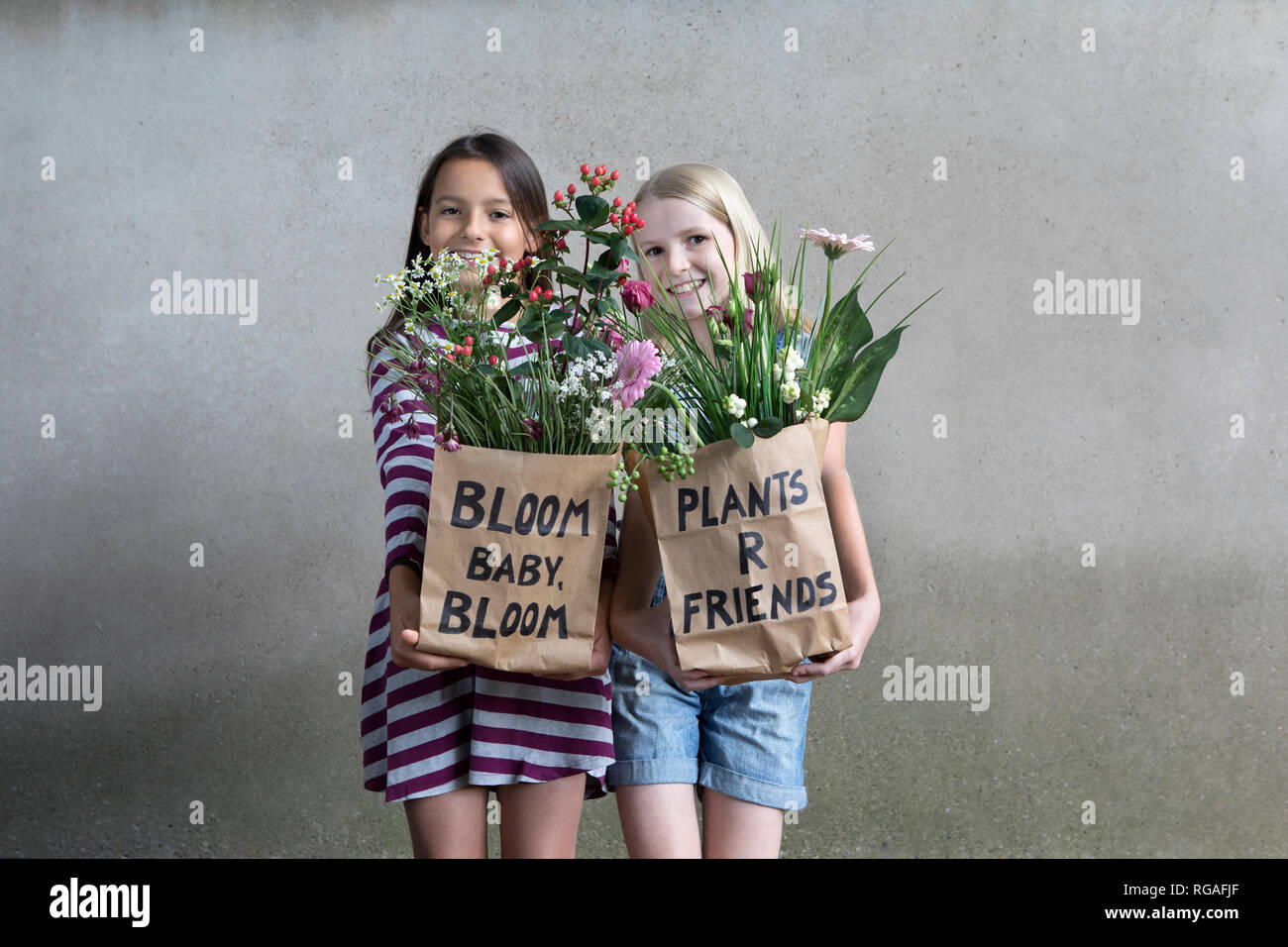 Portrait of two smiling girls standing side by side offering paper bags with flowers Stock Photo