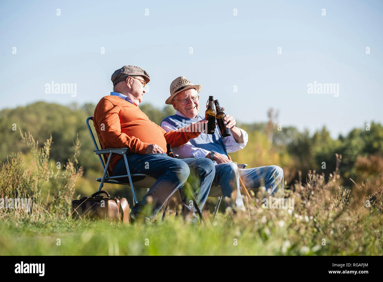 Two old friends sitting in the fields, drinking beer, talking about old times Stock Photo