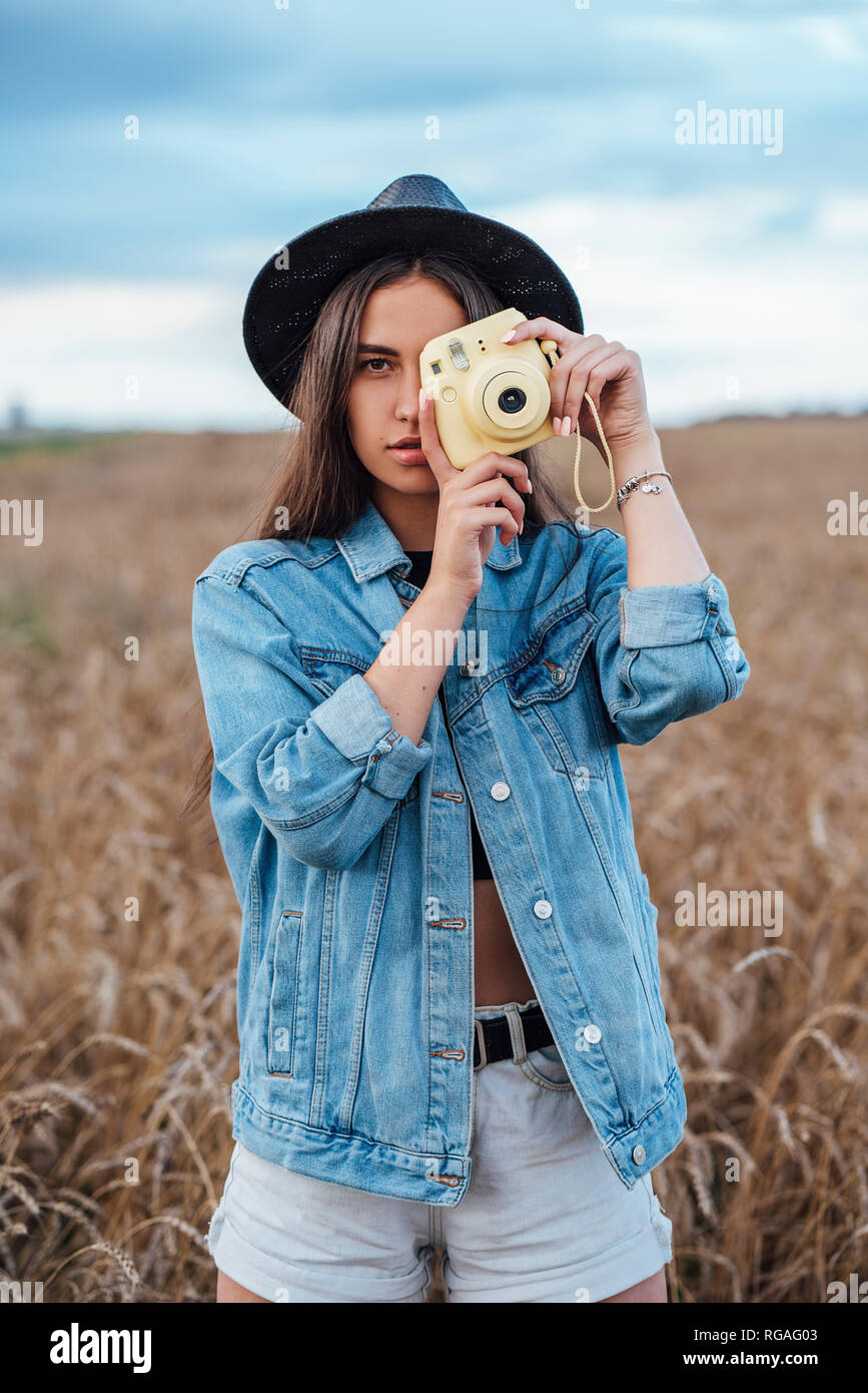 Portrait of young woman wearing hat and denim jacket taking photo of viewer Stock Photo