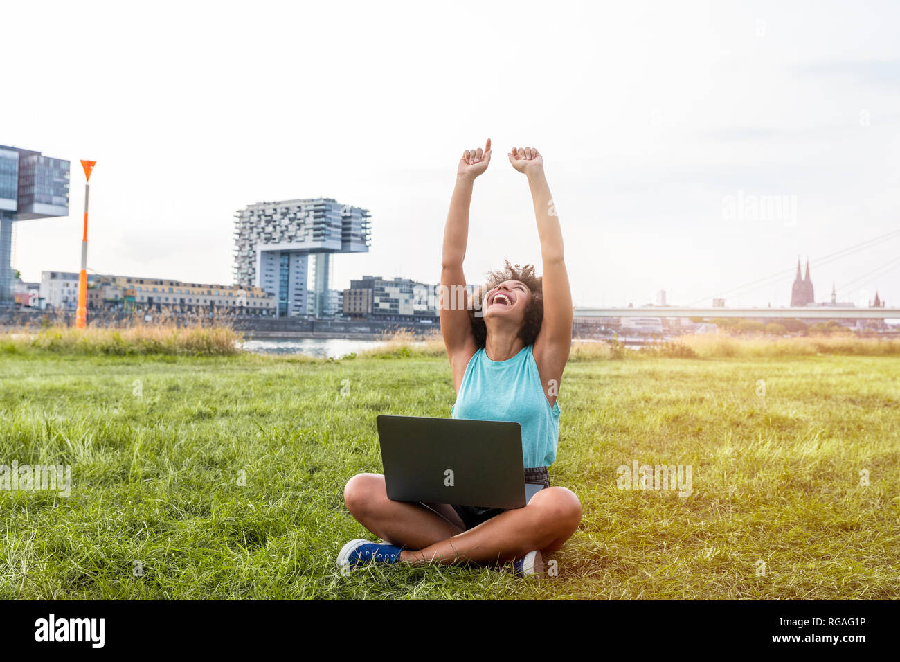 Germany, Cologne, cheering woman sitting on a meadow using laptop Stock Photo