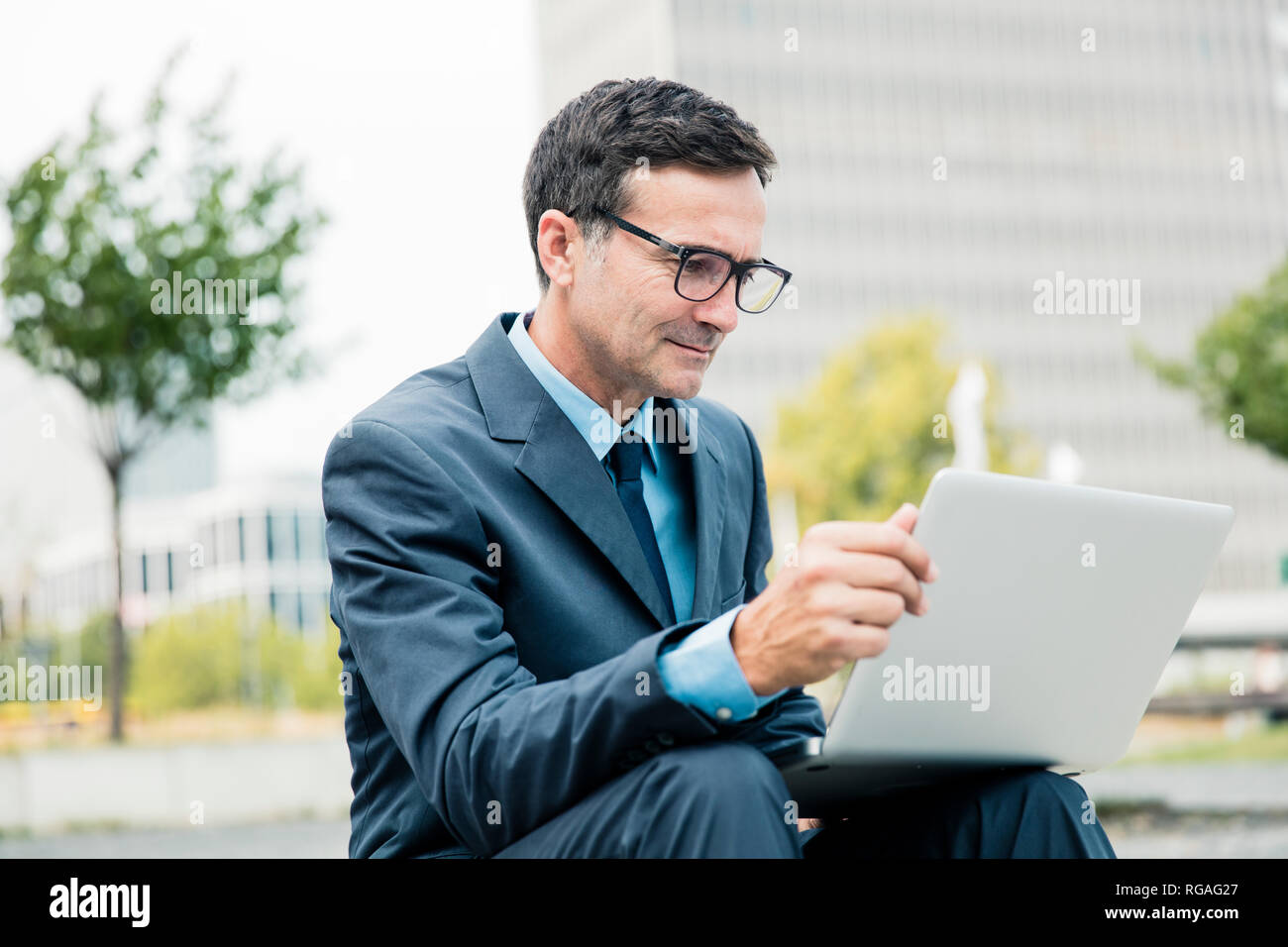 Businessman sitting down using laptop in the city Stock Photo