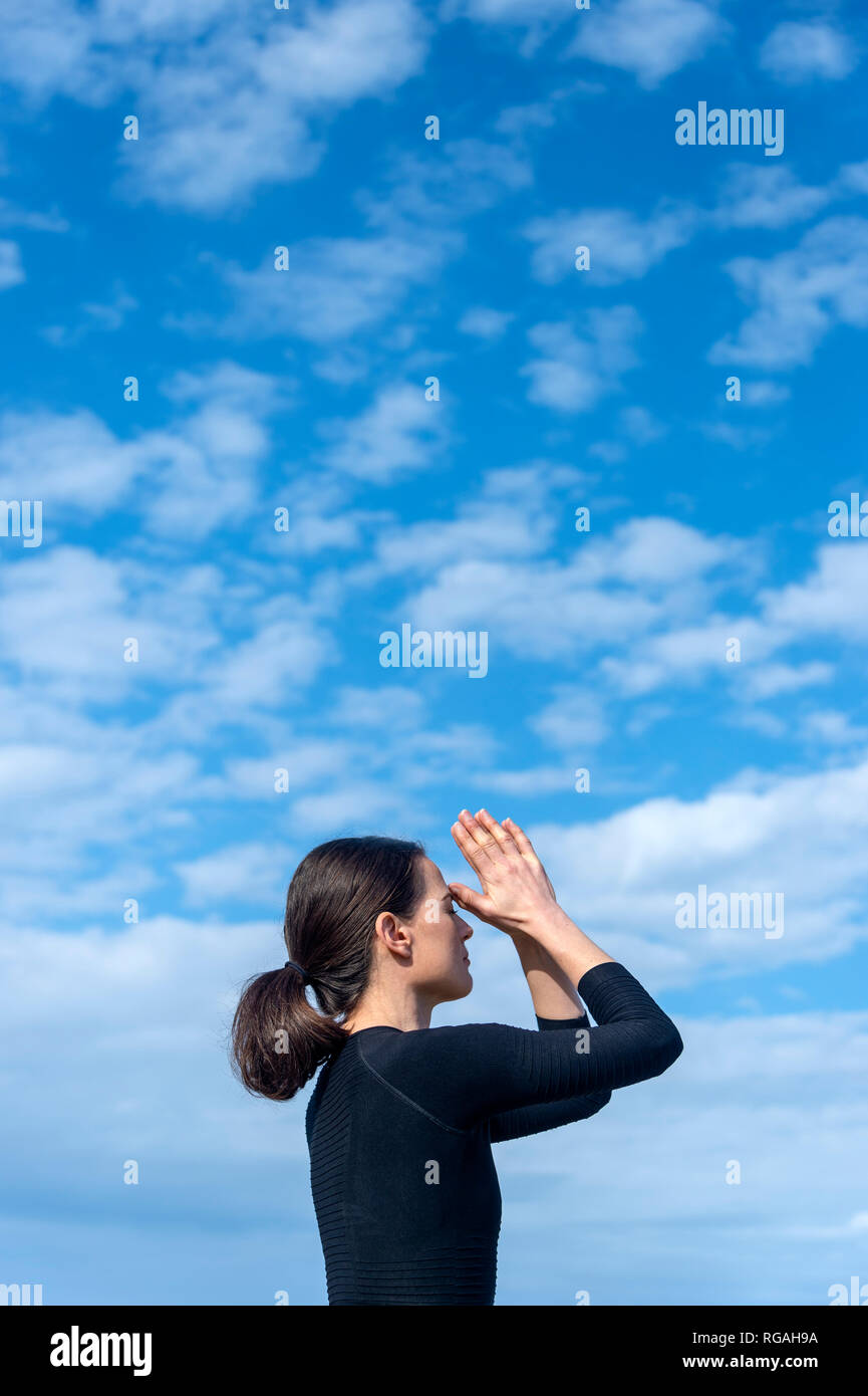 spiritual woman in yoga meditation third eye pose with blue sky backdrop Stock Photo