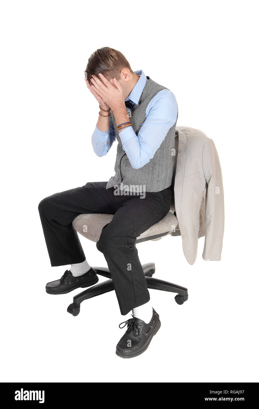 A depressed man in a gray vest sitting on a chair with both hands over  his face is frustrated about his situation, isolated for white background Stock Photo