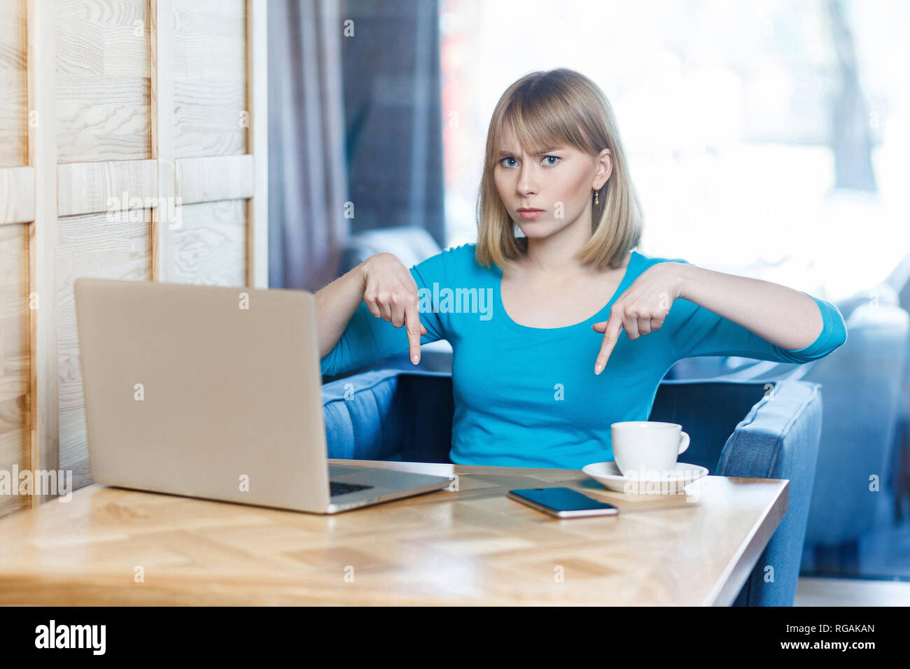 Here and now! Portrait of angry unhappy young businesswoman in blue blouse are sitting in cafe and having bad mood are showing finger up down with ups Stock Photo