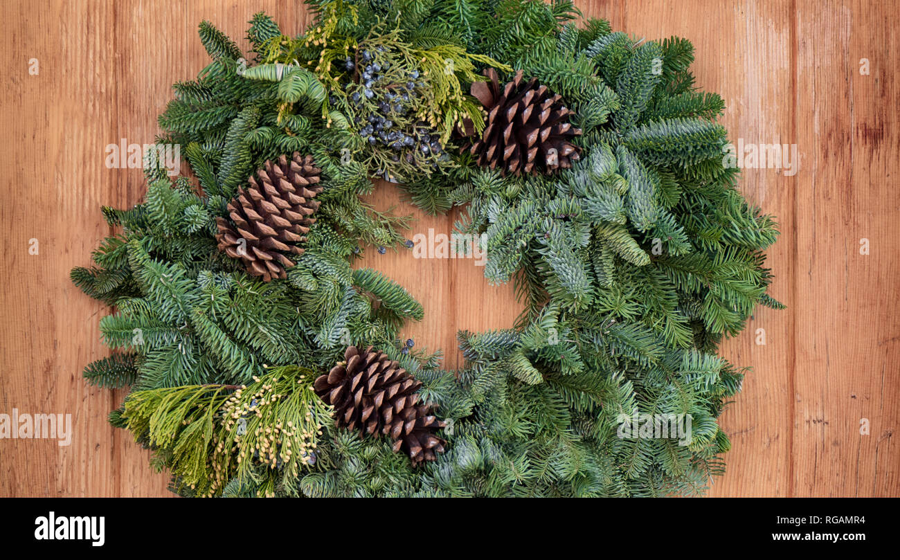 A simple festive evergreen wreath hanging on a wooden door. Stock Photo