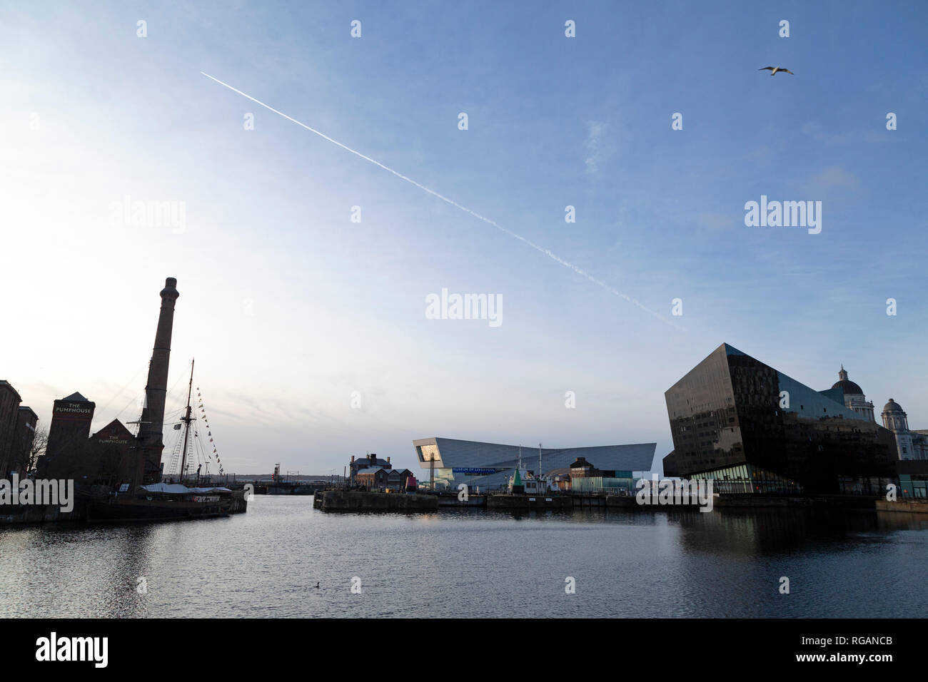 A vapour trail in the sky above the Museum of Liverpool and RIBA North in Liverpool, England. The buildings are seen across the water of the Canning D Stock Photo