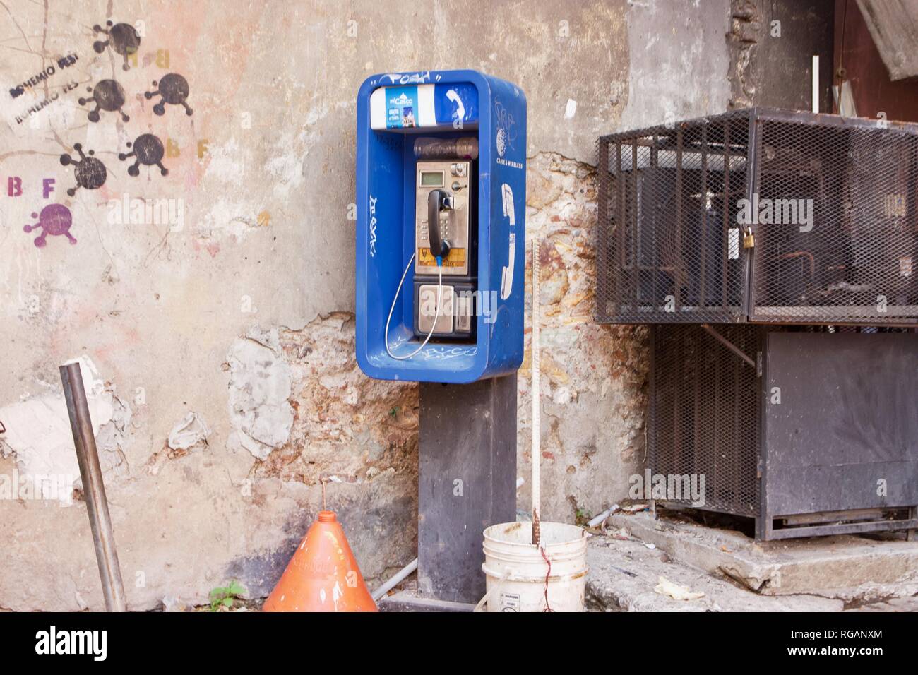 A blue public payphone or public telephone surrounded by graffiti in an urban setting Stock Photo