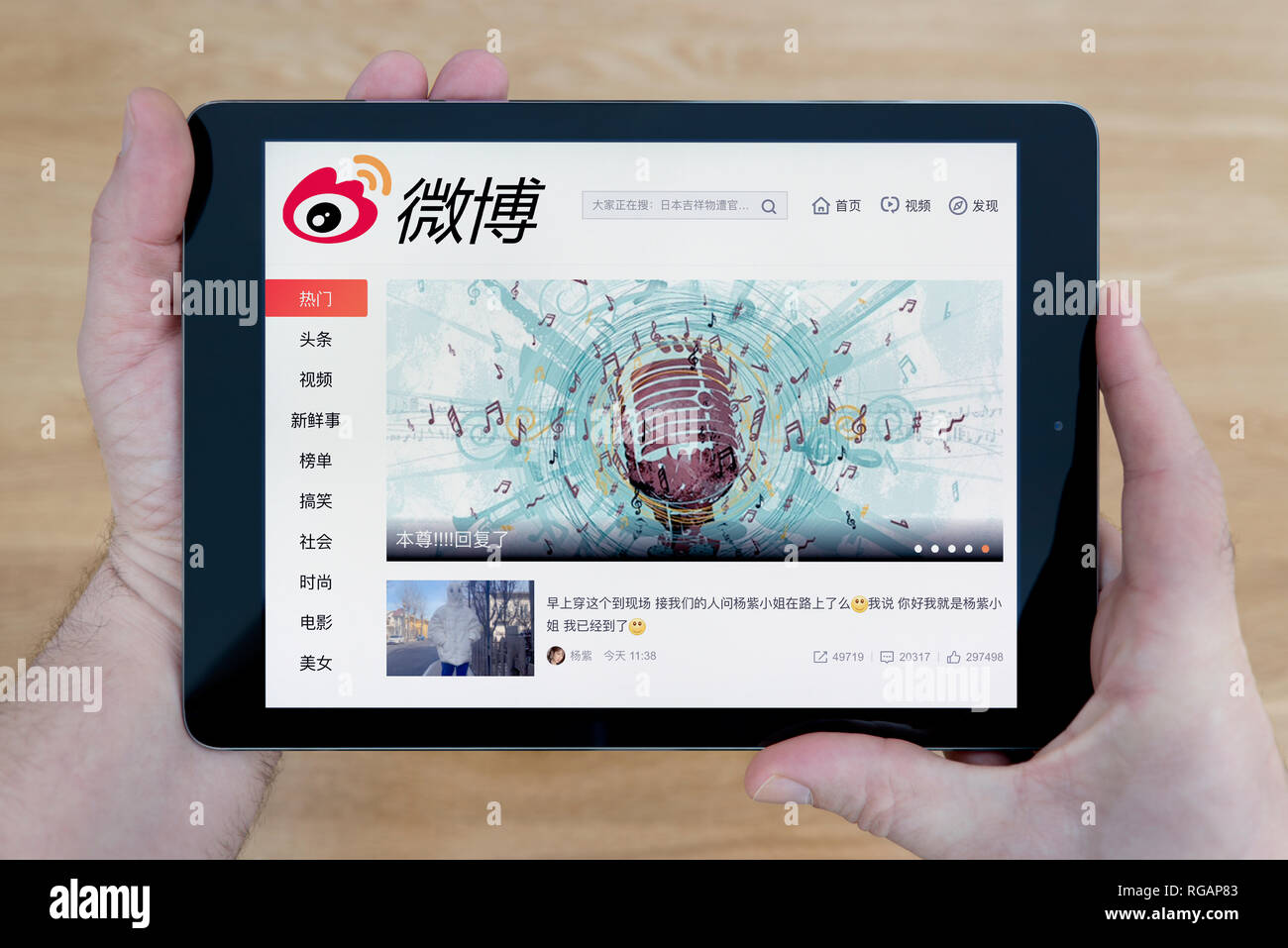 A man looks at the Weibo website on his iPad tablet device, shot against a wooden table top background (Editorial use only) Stock Photo