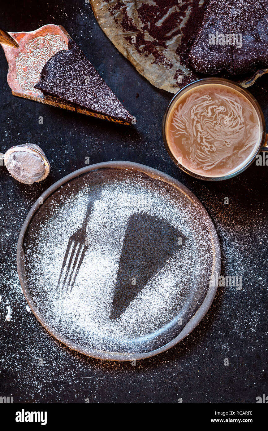 Imprint of a slice of cake and a fork, made with powdered sugar, mug of coffee, chocolate cake Stock Photo