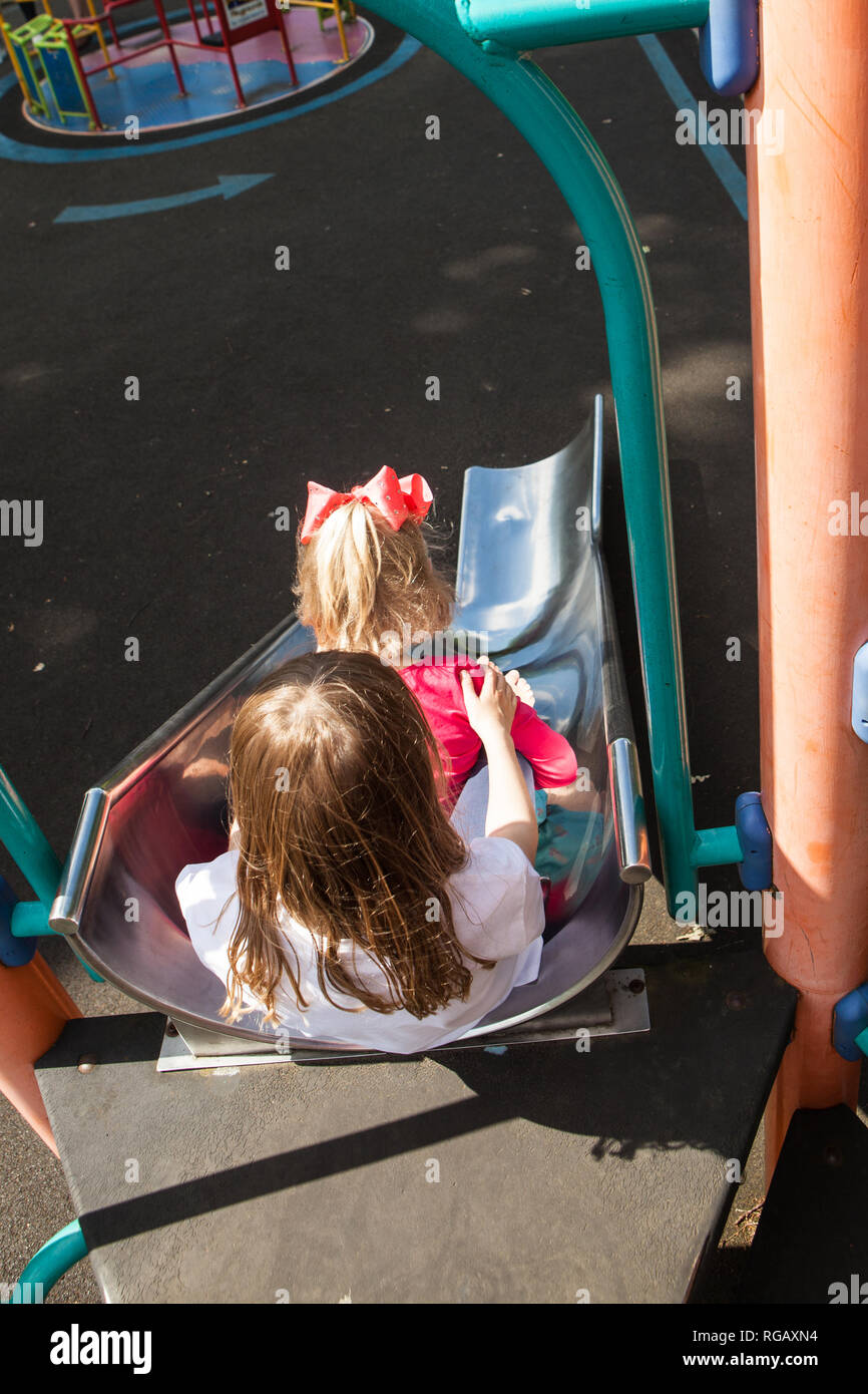 two caucasion girls on a slide in a playground Stock Photo - Alamy