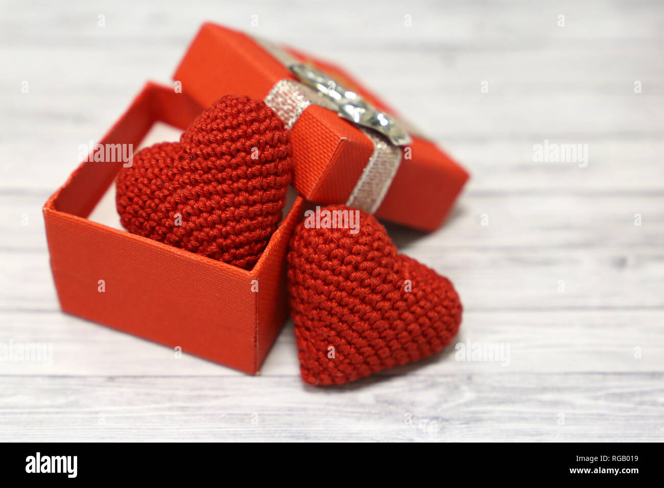 Valentine gift box with red knitted hearts on light wooden table. Romantic present in Valentine's day, wedding concept, love hearts Stock Photo
