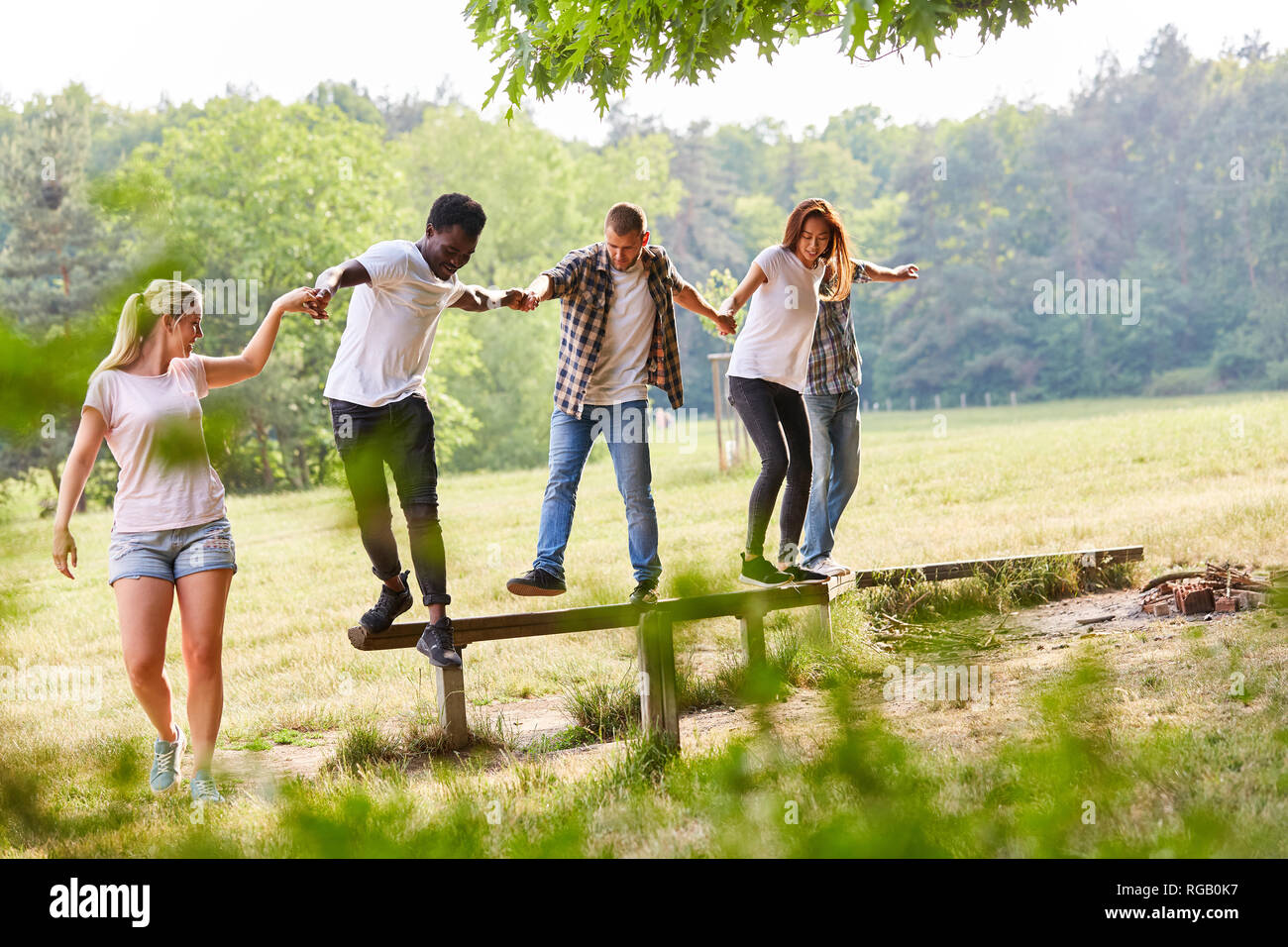 Group of young people exercises teamwork while balancing on a balance beam Stock Photo