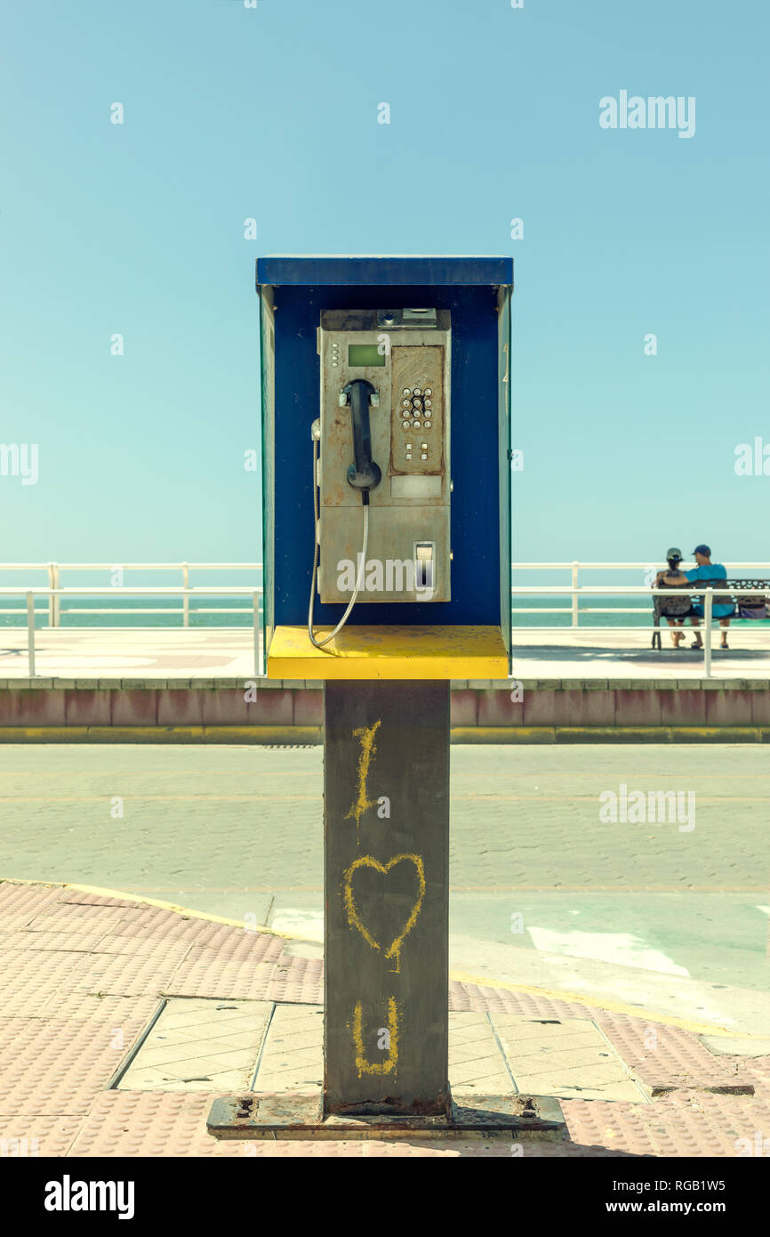 Dirty and disused phone booth with romantic graffiti and a couple in the background. Stock Photo