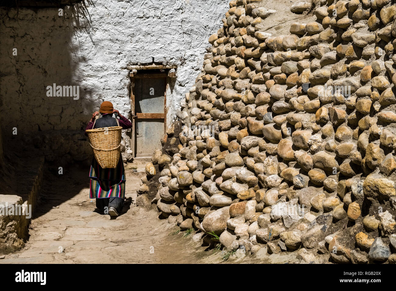 Small alley between white painted traditional houses and rock walls inside the walled town, a local woman carrying a basket Stock Photo