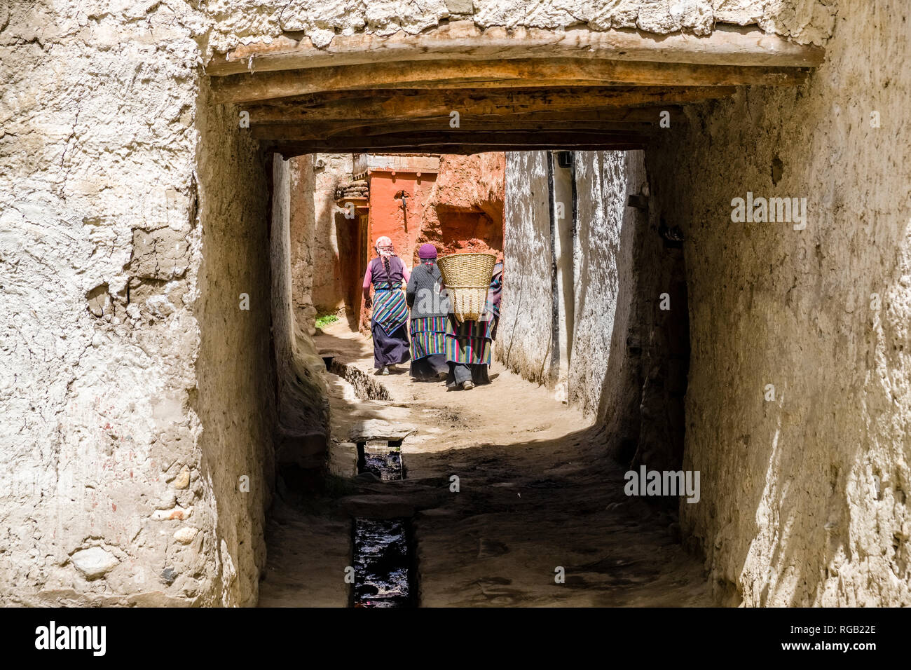 Small alley between white painted traditional houses and rock walls inside the walled town, some local women carrying baskets Stock Photo