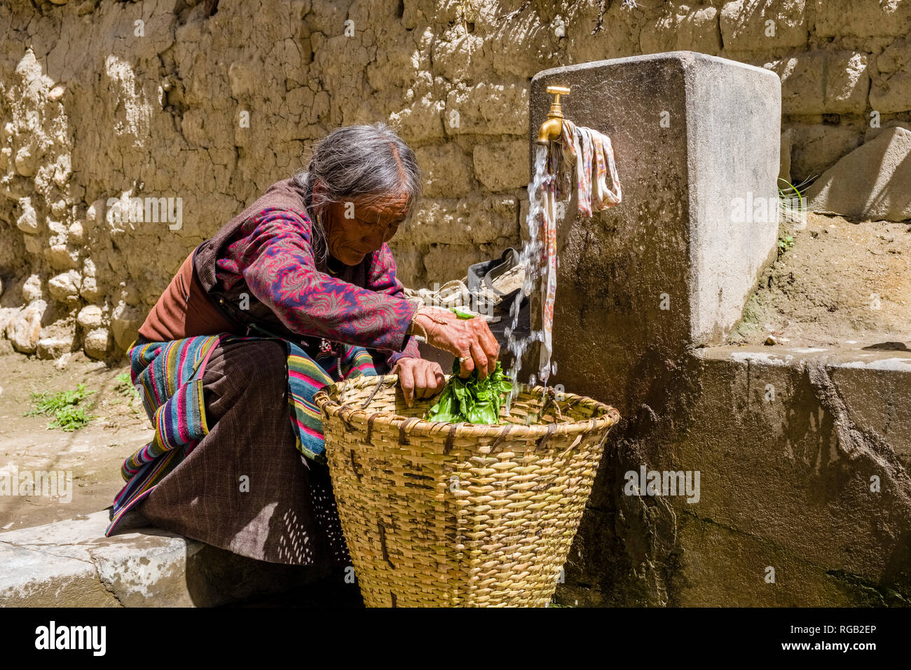 A local woman is cleaning vegetables in a basket at a water tab inside the walled town Stock Photo