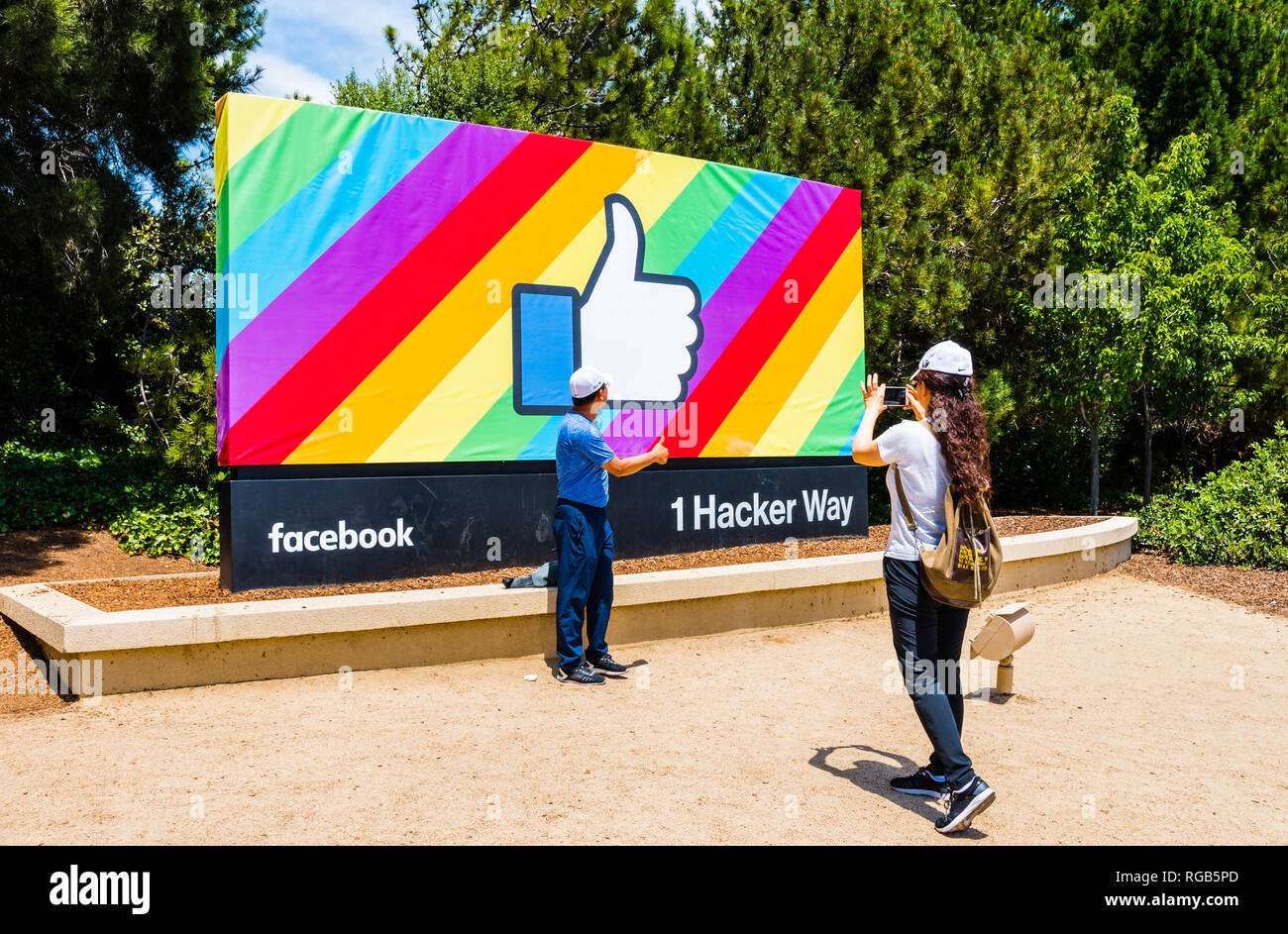 June 18, 2018 Menlo Park / CA / USA - Visitors posing in front of the Facebook Like Button; Rainbow flag background, celebrating LGBTQ pride month; en Stock Photo