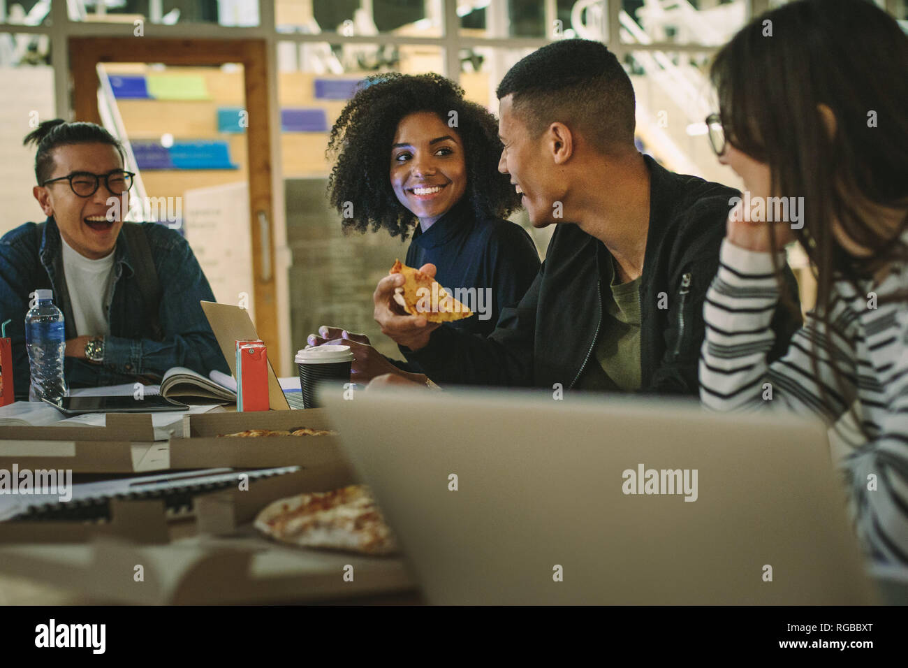 Group of students eating pizza at college canteen. Multi-ethnic men and women students eating at university campus cafe. Stock Photo